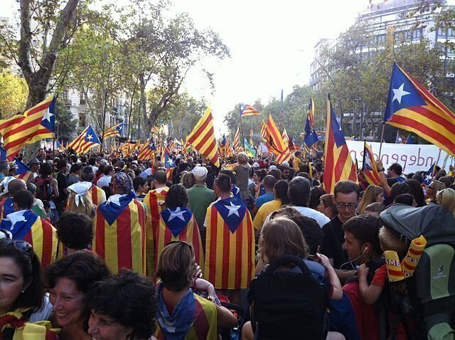 group of people with flags of Catalan Spain draped over shoulders and on poles held above crowd