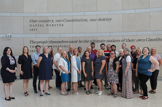 Group of teachers standing together in front of granite wall in the National Constitution Center with engraved quotes by Daniel Webster and Theodore Roosevelt.