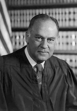 Justice Potter Stewart, head and shoulders portrait, in front of flag and bookcase, by Robert S. Oakes, photographer, 1976.